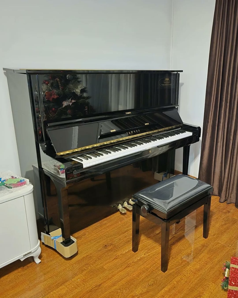 Fekete Yamaha pianínó és egy zongorapad a függöny mellett egy nappaliban
